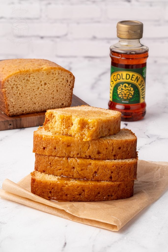 Stack of syrup-drizzled golden syrup cake slices with a bottle of golden syrup in the background.